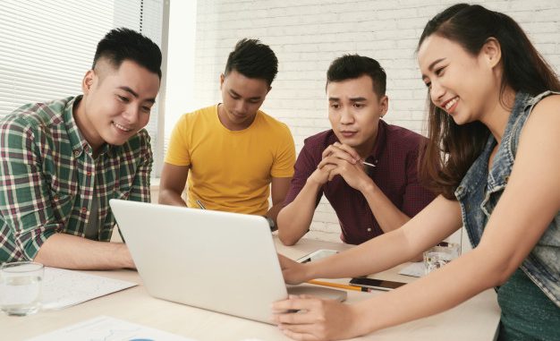 group-casually-dressed-young-asian-people-standing-around-table-looking-laptop-screen_1098-18618